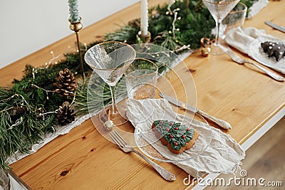 Stylish Christmas table setting. Christmas tree cookie on plate, linen napkin with bell, vintage cutlery, wineglass, fir branches Stock Photo