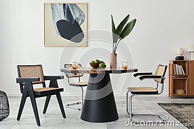 Stylish composition of dining room interior with design table, modern chairs, decoration, tropical leaf in vase, fruits, bookcase. Stock Photo
