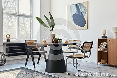 Stylish composition of dining room interior with design table, modern chairs, decoration, tropical leaf in vase, fruits, bookcase. Stock Photo