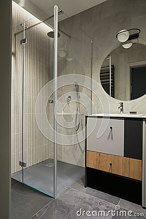 Stylish composition of modern bathroom interior. Designed shower, mixed wood commode, mirror and personal accessories. Walls with Stock Photo