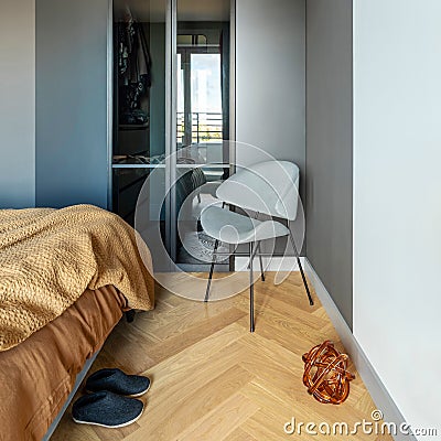 Stylish composition of modern bedroom interior. Wardrobe , grey chair and elegant personal accessories. Grey wall. Brown sheeets. Stock Photo