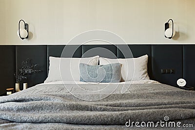 Stylish composition of small modern bedroom interior. Bed, creative lamp and elegant personal accessories. Walls with black panel. Stock Photo