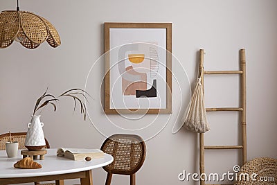 The stylish dining room with round table, rattan chair, wooden commode, pock up poster and kitchen accessories. Beige wall with Stock Photo