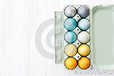 Stylish Easter eggs in carton tray on white wooden background, space for text. Modern colorful easter eggs painted with pastel Stock Photo