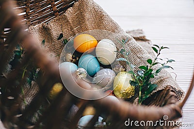 Stylish easter eggs on cloth in rustic basket on white wooden background. Easter hunt concept. Modern easter eggs painted with Stock Photo