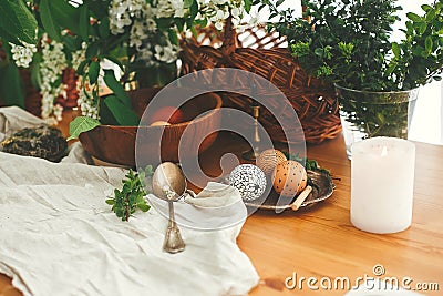 Stylish Easter eggs with modern wax ornaments and natural dyed eggs on rustic wooden table with spring flowers, basket, candle, Stock Photo