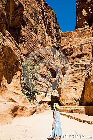 Stylish female tourist in trendy hat and sky-blue dress explore canyon Siq leading to The Treasury, Al Khazneh. Travel and Stock Photo