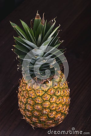 Stylish Fresh Pineapple being seen from a the top on a brown wooden table Stock Photo