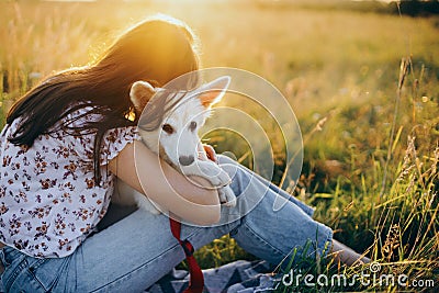 Stylish girl relaxing with her adorable puppy on a picnic. Loyal friend. Happy woman hugging cute white puppy in summer meadow in Stock Photo
