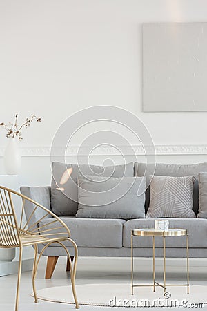 Stylish golden armchair and coffee table in front of grey comfortable sofa with pillows, copy space on empty white wall Stock Photo