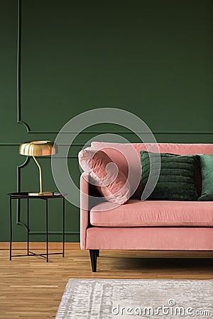 Stylish golden lamp on industrial table next to pink couch with emerald pillows in dark green living room interior,copy space on Stock Photo