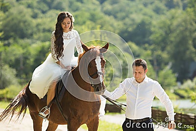 Stylish gorgeous happy brunette bride riding a horse and elegant Stock Photo