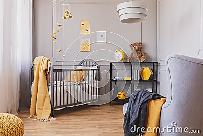 Stylish grey and yellow baby bedroom with crib and industrial black metal shelf Stock Photo