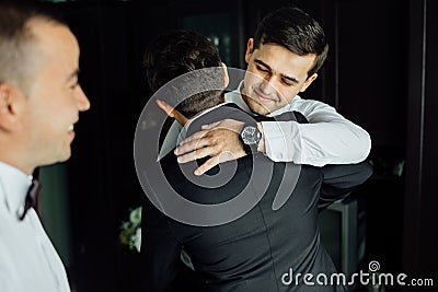 Stylish groomsmen helping happy groom getting ready in the morning for wedding ceremony. Stock Photo