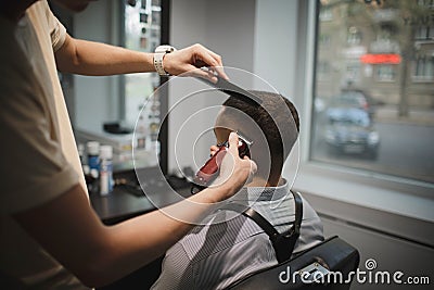 A stylish hairstylist serving client on a barbershop background. Hairdresser`s hands shaving male client`s head. Beauty Stock Photo