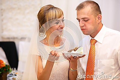 stylish happy bride and groom cutting and tasting fabulous wedding cake in a restaurant Stock Photo