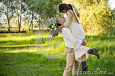 Stylish happy bride, groom hold picked up in hands and dancing. The groom raised and spins bride. Newlyweds kissing. On Stock Photo