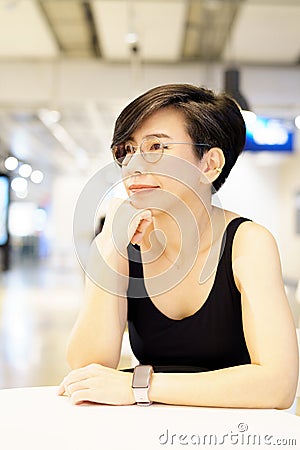 Stylish middle-age Asian woman sitting, thinking, smiling with hand on chin in modern cafe Stock Photo