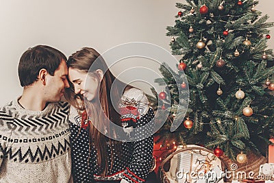 stylish hipster couple in sweaters hugging and embracing at christmas tree in cozy evening room. atmospheric moments. merry chris Stock Photo
