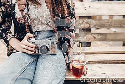 stylish hipster woman holding lemonade and old photo camera. boho girl in denim and bohemian clothes, holding cocktail sitting on Stock Photo