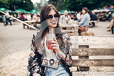 stylish hipster woman in sunglasses with lemonade, smiling. boho girl in denim and bohemian clothes, holding cocktail sitting on Stock Photo
