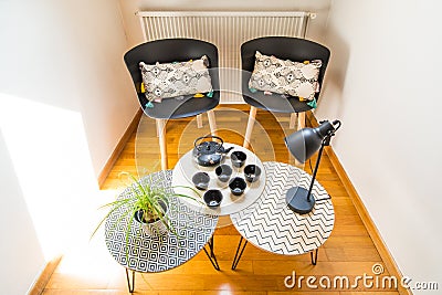 Stylish Interior Decoration of a Cosy Corner of a House with Cast Iron Teapot, Cups, Geometric Tables and Chairs Stock Photo