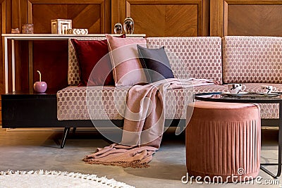 Stylish interior of living room with design pink velvet sofa, elegant pouf, coffee table, plant, pillows, decorations. Stock Photo