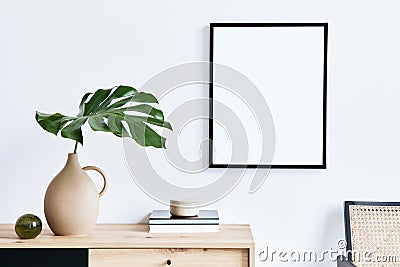Stylish interior of living room with mock up poster frame, wooden commode, book, tropical leaf in ceramic vase and elegant. Stock Photo