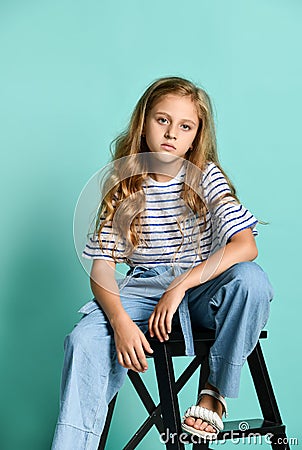 Stylish little girl child wearing summer or autumn jeans clothes sitting on a high chair in the studio Stock Photo