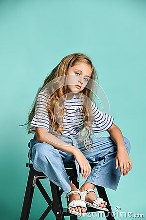 Stylish little girl child wearing summer or autumn jeans clothes sitting on a high chair in the studio. Stock Photo