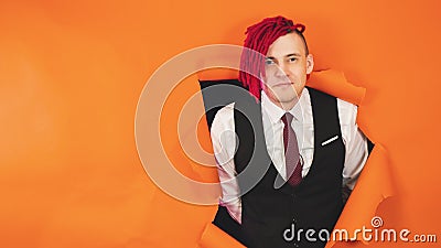 Smiling man with red dreadlocks in hole in wall. Stylish male with bright dreadlocks looking at camera through hole in Stock Photo