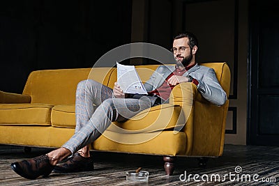 stylish man reading newspaper and sitting on couch, ashtray with cigar Stock Photo