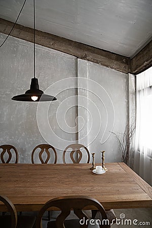 Stylish modern loft dining area with natural light scene and bare concrete wall with natural wood table and chairs setting / Stock Photo