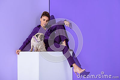 stylish mulatto girl in purple suit sitting on cube with pug dog, ultra violet Stock Photo