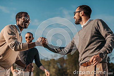 Stylish multicultural friends shaking hands while playing golf on golf course Stock Photo