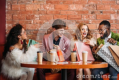 stylish multiethnic young people looking into shopping bags while drinking coffee Stock Photo