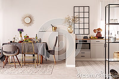 Stylish open plan kitchen and dining room interior with white cupboard and long table with grey tablecloth and food Stock Photo