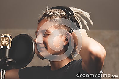 Stylish positive guy with dreadlocks is recording a song in the studio. A young attractive singer in black studio headphones Stock Photo