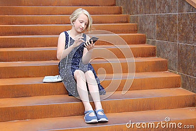 Stylish preteen girl using a phone sitting on a rusty staircase. Child and gadget concept. Stock Photo