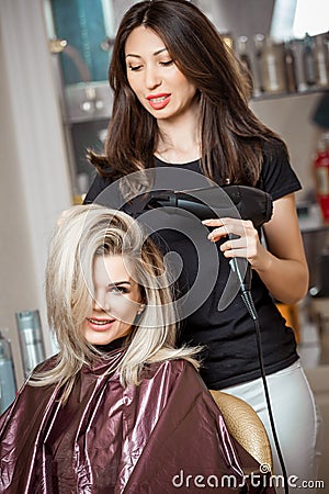 Stylish professional, hairdresser doing hairdoing to the client with a hair dryer on the background of the hairdresser`s Stock Photo