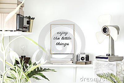 Stylish scandinavian interior with white shelf, golden mock up poster frame, books, hourglass, camera, windmill and vintage radio. Stock Photo