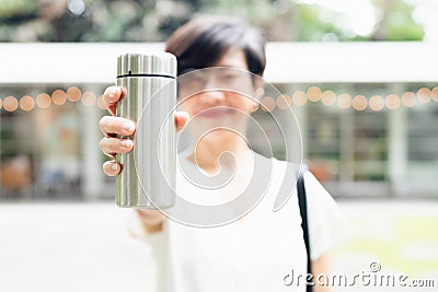 Stylish short hairstyle Asian woman holding, showing reusable insulated stainless steel water bottle, smile, Stock Photo
