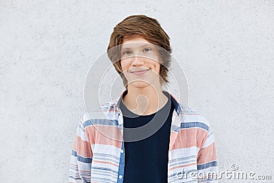 Stylish teenage boy with trendy hairstyle having dark eyes, pure skin and dimples on cheeks wearing shirt standing against white c Stock Photo