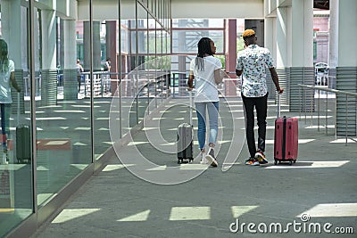 Stylish tourist black couple with suitcases walking along street near by the station and talking Stock Photo