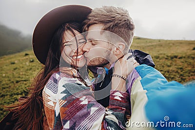 stylish traveler couple taking selfie photo in mountains. hipster man and woman with windy hair in hat smiling and kissing. space Stock Photo