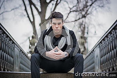 Stylish trendy young man sitting outdoor on old metal bridge Stock Photo