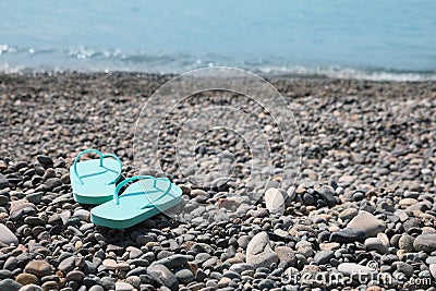 Stylish turquoise flip lops on pebble beach near sea. Space for text Stock Photo