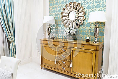Stylish Vintage Style Home Interior with Wooden Commode and Decorated Mirror. Symmetrical Reading Lamps on Commode Stock Photo