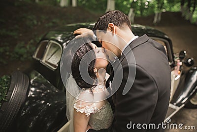 Stylish wedding couple, bride, groom kissing and hugging near retro car in autumn Stock Photo