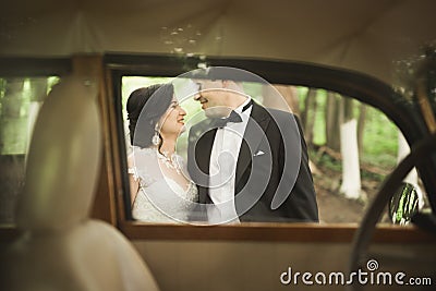 Stylish wedding couple, bride, groom kissing and hugging near retro car in autumn Stock Photo